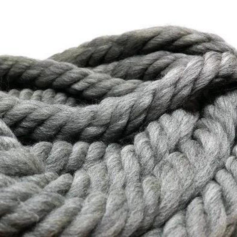 A close-up of a thick, gray rope made of yarn. The chunky yarn is twisted, creating a textured and interesting texture.