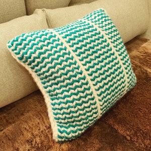 May include: A teal and white patterned throw pillow with a chevron design. The pillow is made of a soft, woven fabric.