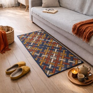 A blue, orange, and white geometric patterned rug with a woven texture. The rug is placed in front of a gray couch.