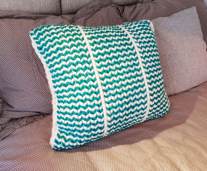 May include: A teal and white chevron patterned throw pillow with three white stripes down the center.