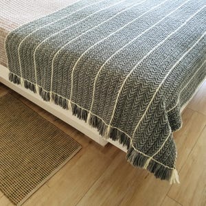 A gray and white striped throw blanket with fringe on the edges. The blanket is draped over a bed.
