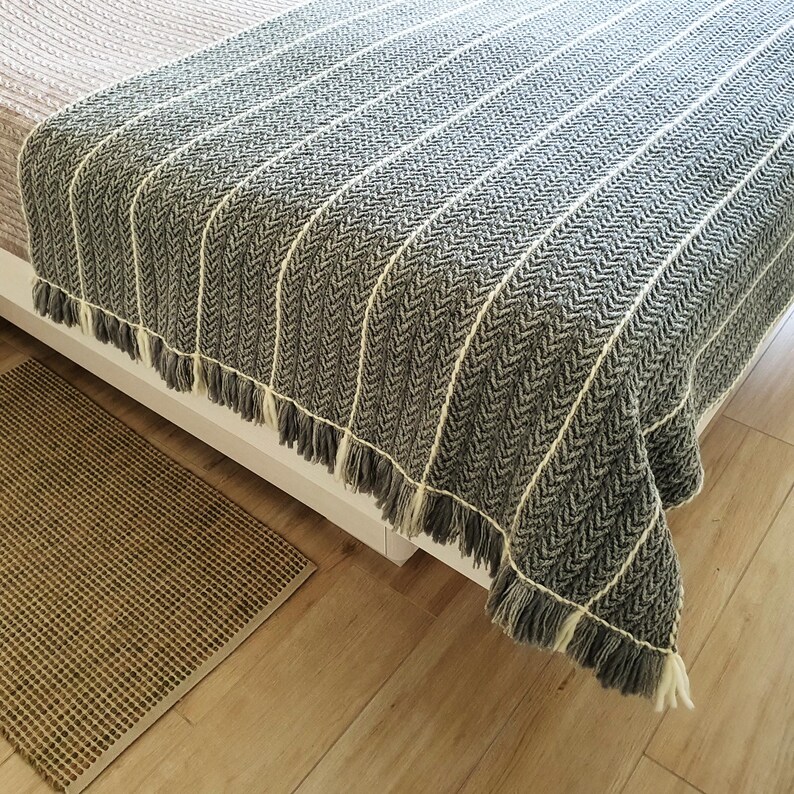 A gray and white striped throw blanket with fringe on the edges. The blanket is draped over a bed.