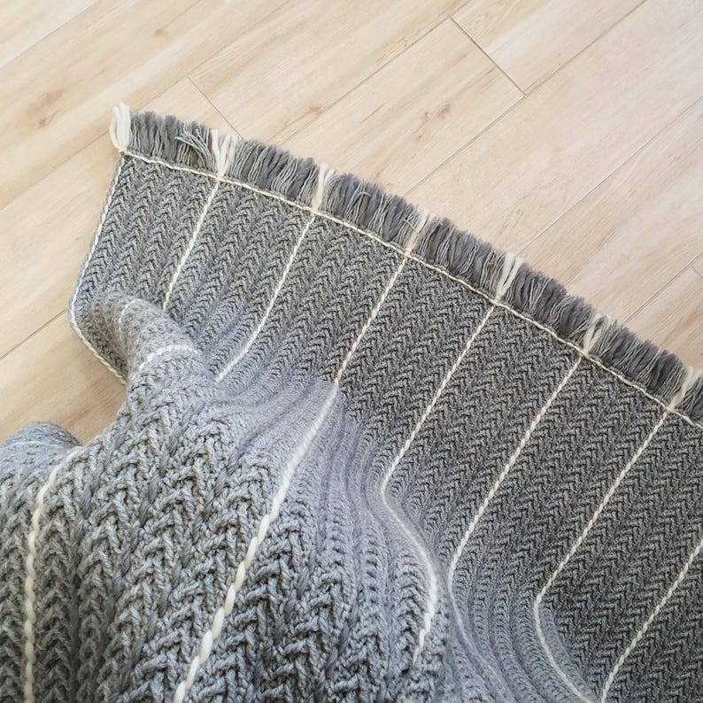 Close-up of grey crochet texture with thin white wool pinstripes and soft fringe detail. Natural wool fiber quality.