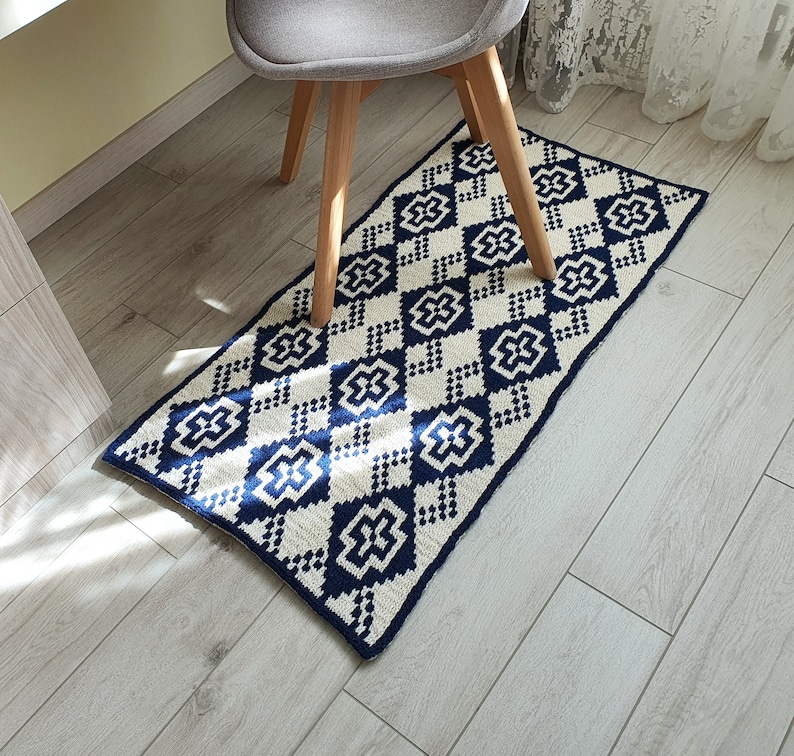 May include: A white and navy blue geometric patterned rug with a diamond design. The rug is made of a soft, woven material and has a subtle sheen.