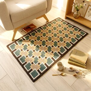 Handmade wool rug in Beige, Brown, Green and Teal tones placed beside an armchair, geometric pattern visible, soft natural light