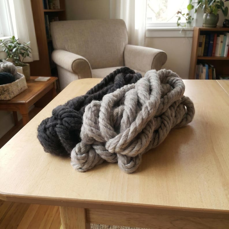 Two skeins of the chunky wool yarn in different colors: gray and anthracite on a table in a modern living room.