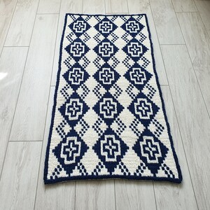 May include: A white and navy blue crocheted rug with a geometric pattern. The rug has a diamond shape with a cross in the center of each diamond.