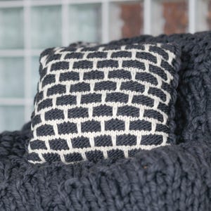 Modern farmhouse living room decor with black and white knit pillow. Textured wool accent cushion on a leather sofa.