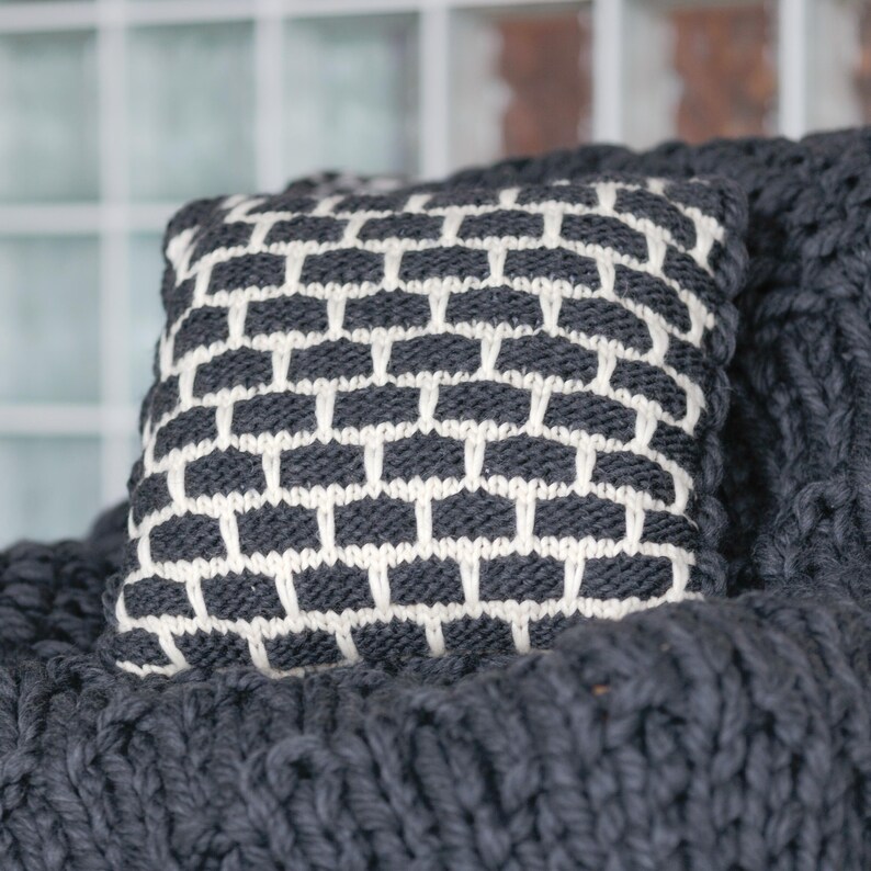 Modern farmhouse living room decor with black and white knit pillow. Textured wool accent cushion on a leather sofa.