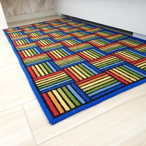 Brightly colored geometric rug placed next to a white modern bed on light wood floor.