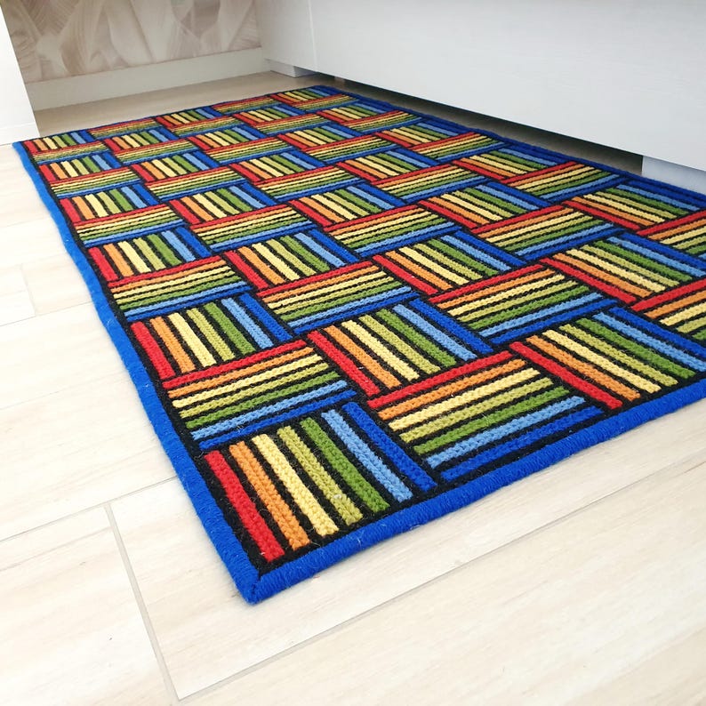Brightly colored geometric rug placed next to a white modern bed on light wood floor.