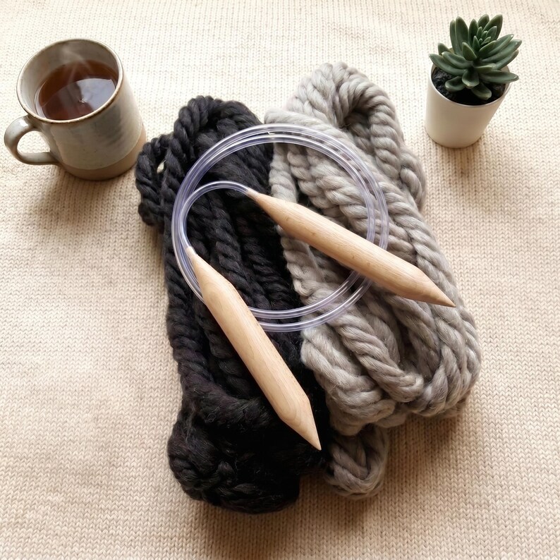 Two skeins of thick wool yarn in different colors: gray and anthracit with wooden knitting needles circular on a table.