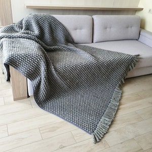 Peut inclure: Une couverture grise textur&eacute;e avec un motif de point de bouloche est drap&eacute;e sur un canap&eacute; gris clair. La couverture a une frange sur le bord. La couverture est faite d'un mat&eacute;riau doux et est parfaite pour ajouter de la chaleur et de la texture &agrave; un espace de vie.