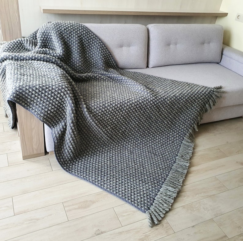 Peut inclure: Une couverture grise textur&eacute;e avec un motif de point de bouloche est drap&eacute;e sur un canap&eacute; gris clair. La couverture a une frange sur le bord. La couverture est faite d'un mat&eacute;riau doux et est parfaite pour ajouter de la chaleur et de la texture &agrave; un espace de vie.