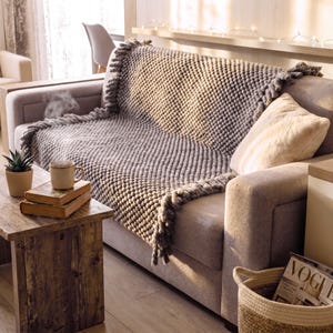 Chunky knit blanket placed on a sofa with relaxed folds and textured surface.