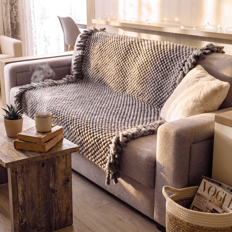 Chunky knit blanket placed on a sofa with relaxed folds and textured surface.