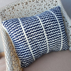 May include: A blue and white chevron patterned throw pillow with a woven texture. The pillow is sitting on a white wicker chair.