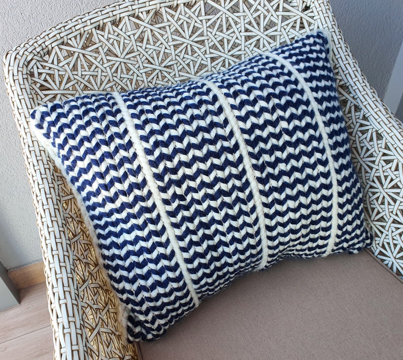 May include: A blue and white chevron patterned throw pillow with a woven texture. The pillow is sitting on a white wicker chair.