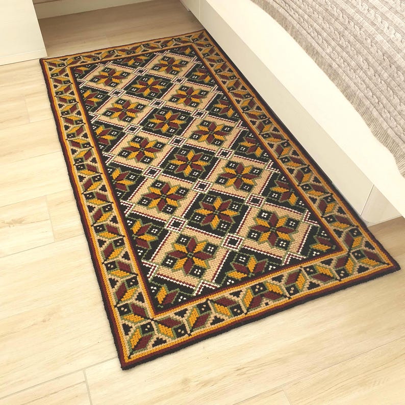 Rectangular rug with a geometric pattern. The rug features a beige background with a repeating pattern of black, yellow, and burgundy folk-like shapes. A border of burgundy, yellow, and green geometric shapes frames the rug.