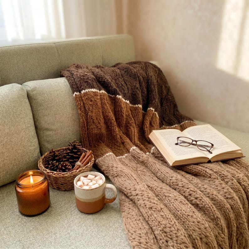 A brown and beige knitted throw blanket with white stripes. The blanket is draped over a couch with books.
