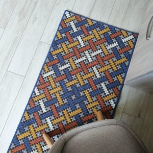 A blue, orange, and white geometric patterned rug with a woven texture. The rug is made of yarn and has a modern design.