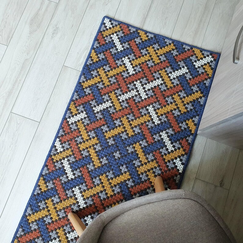 A blue, orange, and white geometric patterned rug with a woven texture. The rug is made of yarn and has a modern design.
