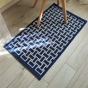 May include: A blue and white geometric patterned rug with a woven design. The rug is on a light wood floor.