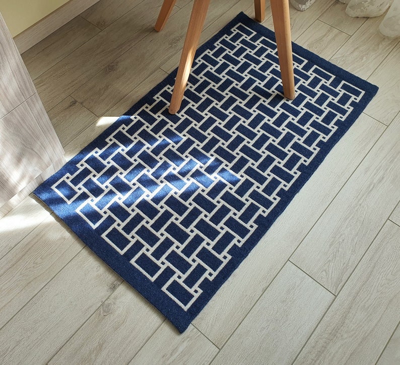 May include: A blue and white geometric patterned rug with a woven design. The rug is on a light wood floor.