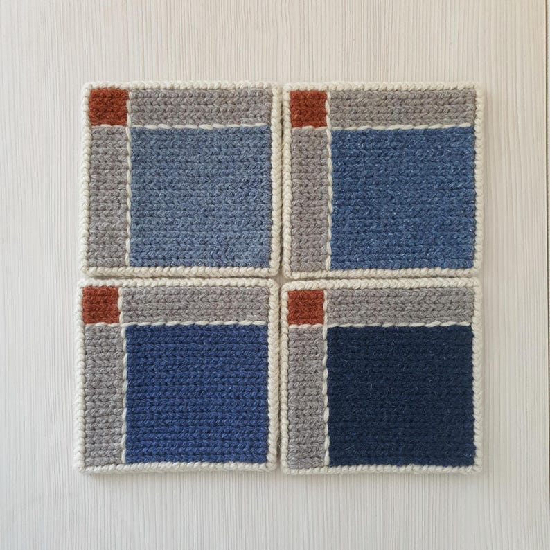 May include: Four square crochet coasters. Each coaster features a blue center, gray border, and a rust-colored square in the corner. The coasters are bordered with a cream-colored yarn.