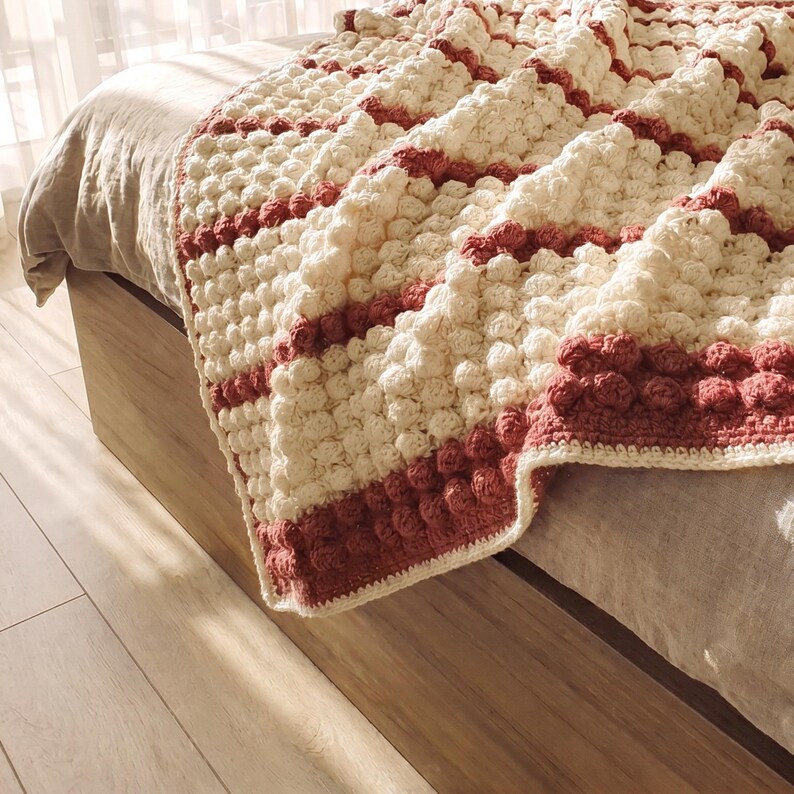 Handmade volumetric crochet woolen blanket handmade on a bed in a bedroom.