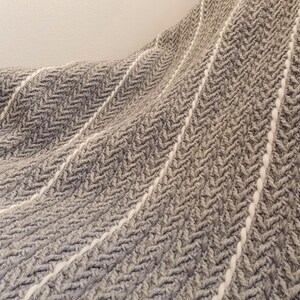 A gray and white woven throw blanket with a herringbone pattern. The blanket has a soft, textured feel.