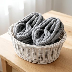 Two gray sckeins of chunky wool yarn in a white basket on a wooden table.