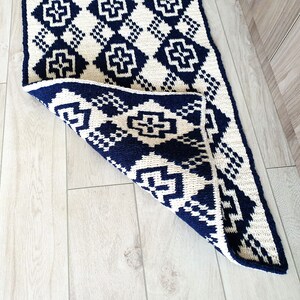 May include: A white and navy blue geometric patterned rug with a diamond pattern. The rug is folded in half and the navy blue side is facing up.