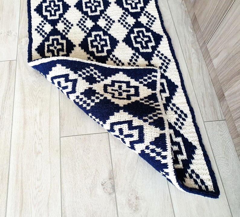May include: A white and navy blue geometric patterned rug with a diamond pattern. The rug is folded in half and the navy blue side is facing up.