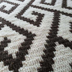 May include: Close-up of a woven rug with a geometric pattern. The rug is made of natural fibers in shades of brown and white.