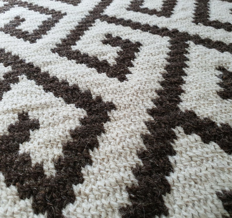 May include: Close-up of a woven rug with a geometric pattern. The rug is made of natural fibers in shades of brown and white.