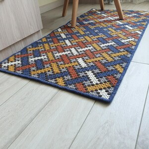 A blue, orange, yellow, and white geometric patterned rug with a crocheted texture.