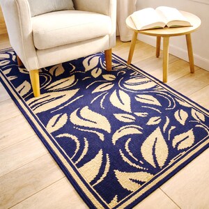 A navy blue and beige patterned rug with a leaf design. The rug has a border of beige and is made of a woven material.