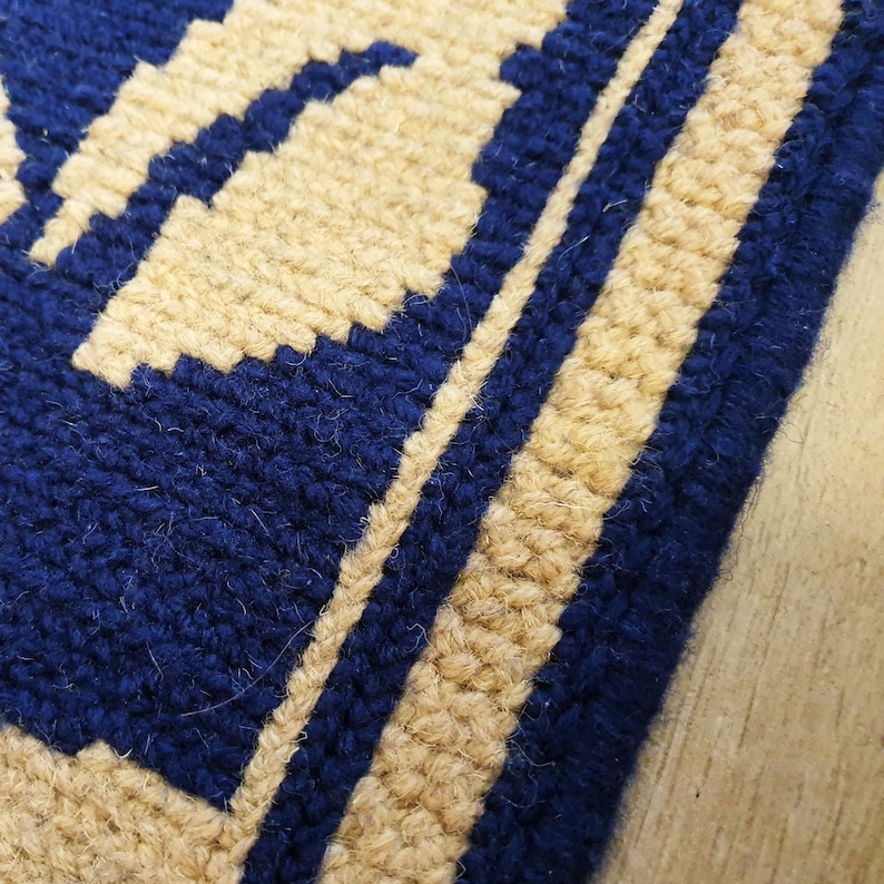 Close-up of a blue and beige woven rug with a geometric pattern. The rug has a fringe border.