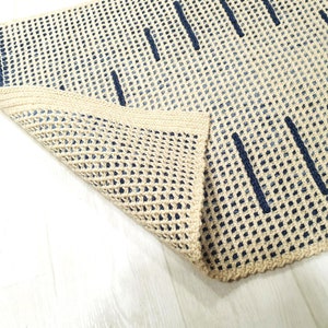 May include: A beige and blue woven rug with a geometric pattern. The rug is folded in half, showing the underside of the rug.