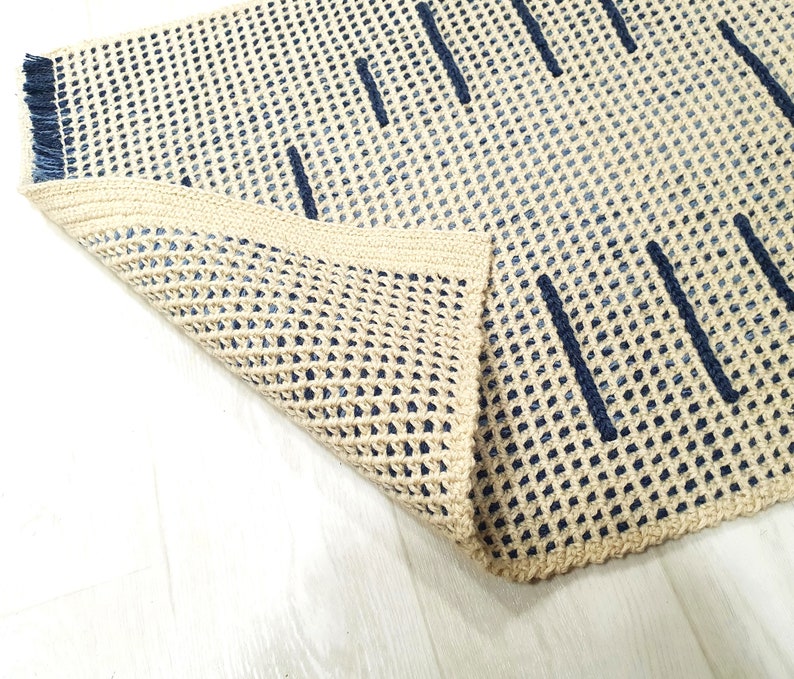 May include: A beige and blue woven rug with a geometric pattern. The rug is folded in half, showing the underside of the rug.