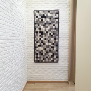 K&ouml;nnte beinhalten: Ein abstrakter Teppich in Schwarzwei&szlig; mit geometrischem Muster h&auml;ngt an einer wei&szlig;en Backsteinwand.