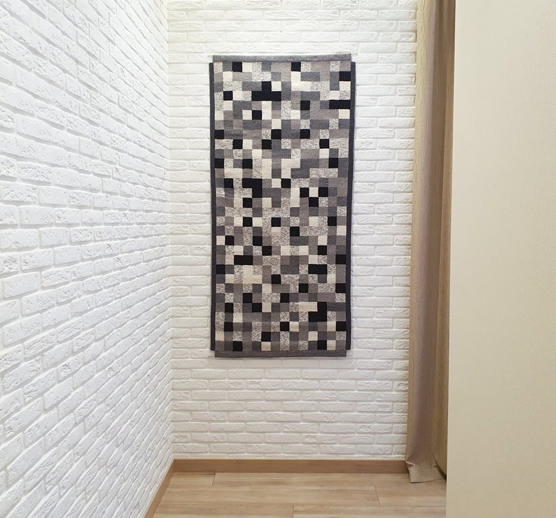 K&ouml;nnte beinhalten: Ein abstrakter Teppich in Schwarzwei&szlig; mit geometrischem Muster h&auml;ngt an einer wei&szlig;en Backsteinwand.