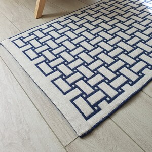 May include: A white and blue geometric patterned rug with a woven texture. The rug has a simple, modern design with a repeating pattern of squares.