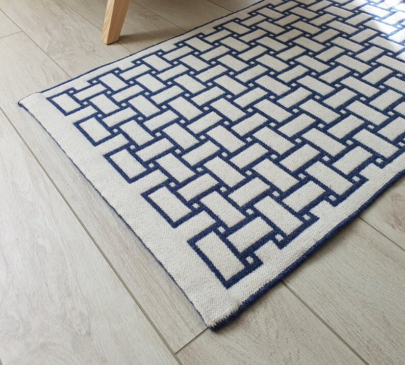 May include: A white and blue geometric patterned rug with a woven texture. The rug has a simple, modern design with a repeating pattern of squares.