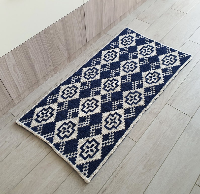 May include: A navy blue and white geometric patterned rug with a diamond pattern. The rug is made of a soft, woven material and has a fringed edge.