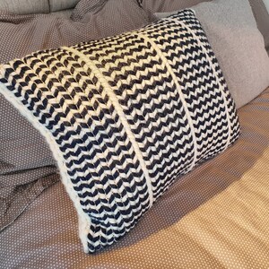 May include: A black and white patterned throw pillow with a chevron design. The pillow is made of a soft, textured fabric and is perfect for adding a touch of style to any room.