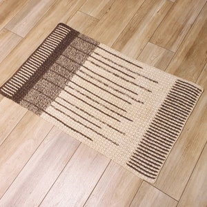 May include: A rectangular brown and cream rug with a striped pattern. The rug has a textured surface and is made of woven fibers.