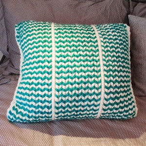 May include: A decorative pillow with a chevron pattern in teal and white. The pillow is made of a woven fabric and has a soft, plush texture.