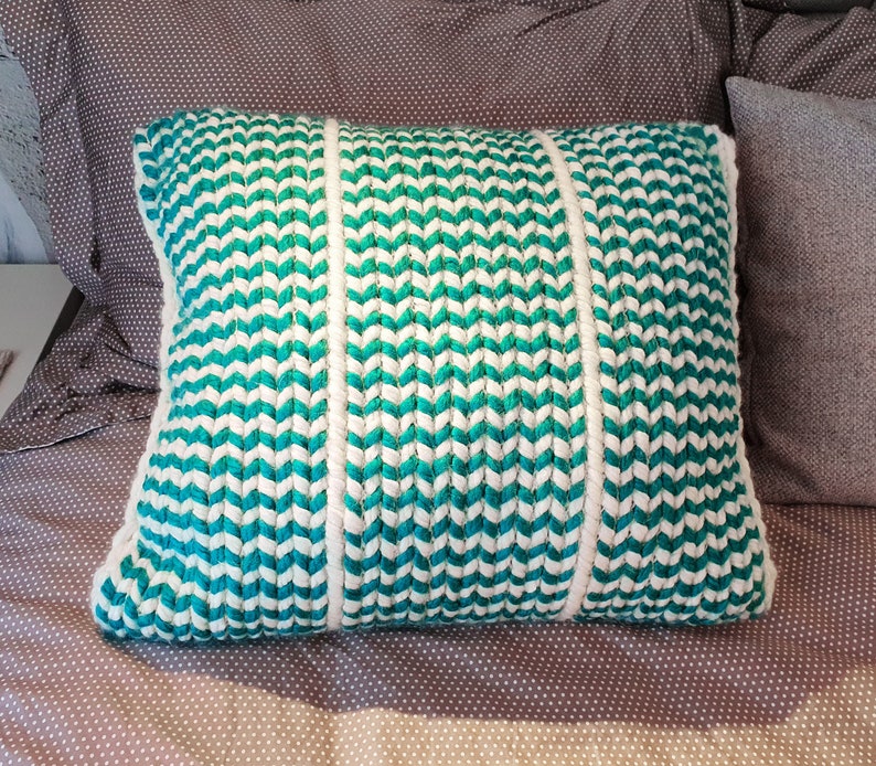 May include: A decorative pillow with a chevron pattern in teal and white. The pillow is made of a woven fabric and has a soft, plush texture.